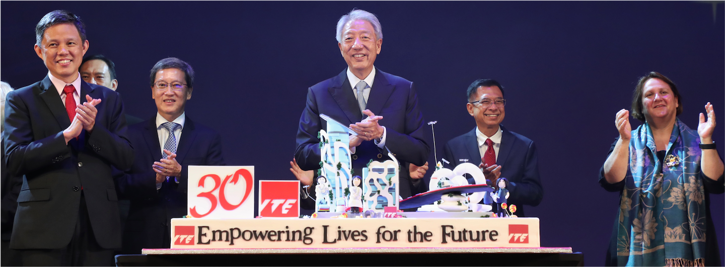 Six people on a stage clapping behind a '30 YTE' cake. "Empowering Lives for the Future."